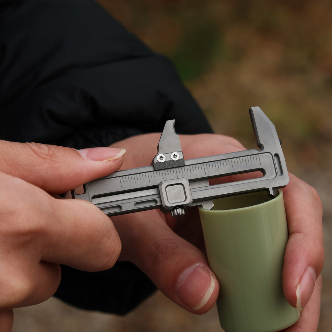 Compact titanium mini caliper measuring a green cylinder, small but tough precision tool for daily carry.