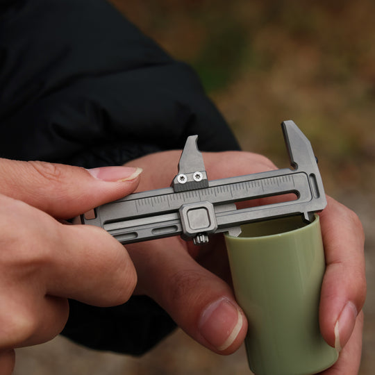 Compact titanium mini caliper measuring a green cylinder, small but tough precision tool for daily carry.