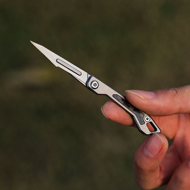 User holding micro titanium folding knife between fingers, showcasing tiny EDC size