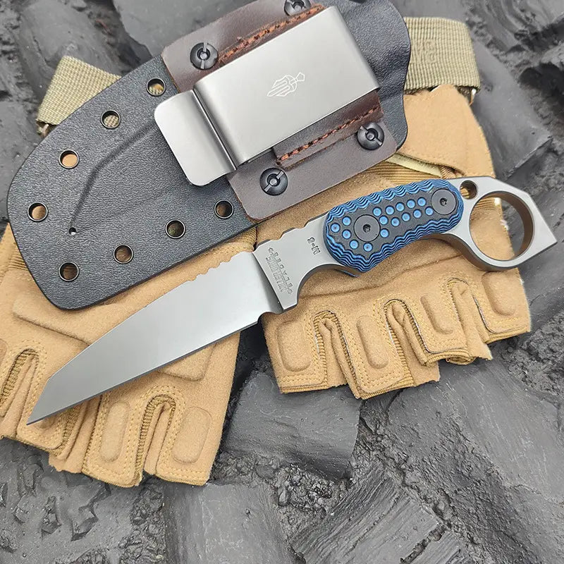 Claw forge tactical knife with blue handle and A2 blade on beige gloves with a sheath in the background